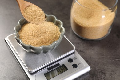 Photo of Putting brown sugar into bowl on digital kitchen scale at grey table, closeup