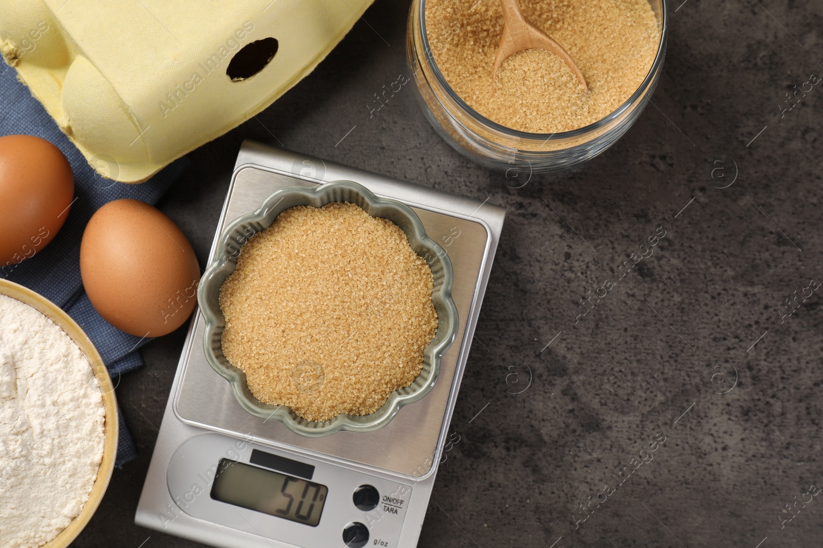 Digital kitchen scale with bowl of flour and other products on grey table, flat lay. Space for text Photo of Digital kitchen scale with bowl of flour and other products on grey table, flat lay. Space for text