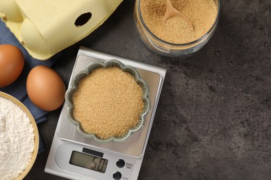 Photo of Digital kitchen scale with bowl of flour and other products on grey table, flat lay. Space for text