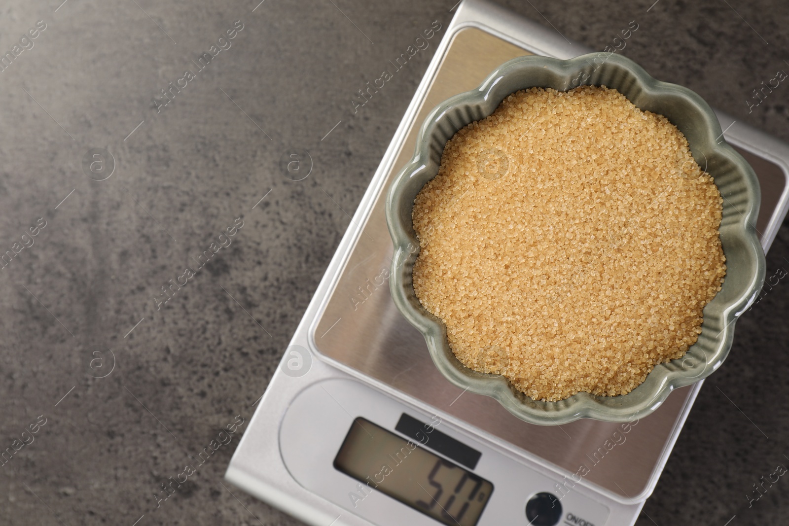 Digital kitchen scale with bowl of brown sugar on grey table, top view. Space for text Photo of Digital kitchen scale with bowl of brown sugar on grey table, top view. Space for text
