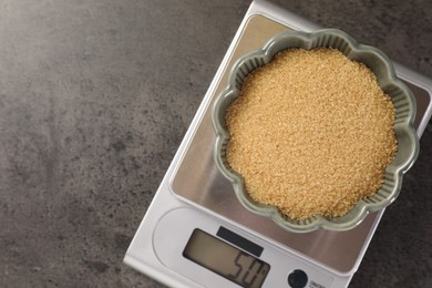 Photo of Digital kitchen scale with bowl of brown sugar on grey table, top view. Space for text