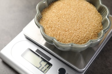 Photo of Digital kitchen scale with bowl of brown sugar on grey table, closeup