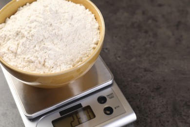 Photo of Digital kitchen scale with bowl of flour on grey table, closeup. Space for text