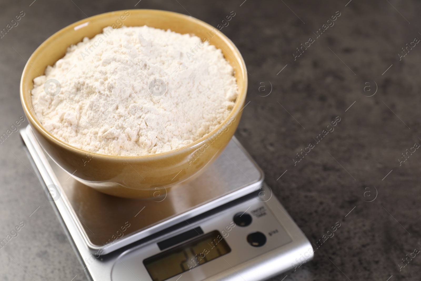 Digital kitchen scale with bowl of flour on grey table, closeup. Space for text Photo of Digital kitchen scale with bowl of flour on grey table, closeup. Space for text