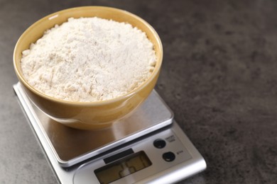 Photo of Digital kitchen scale with bowl of flour on grey table, closeup. Space for text