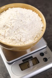 Photo of Digital kitchen scale with bowl of flour on grey table, closeup