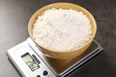 Photo of Digital kitchen scale with bowl of flour on grey table, closeup