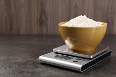 Photo of Digital kitchen scale with bowl of flour on grey table, closeup. Space for text