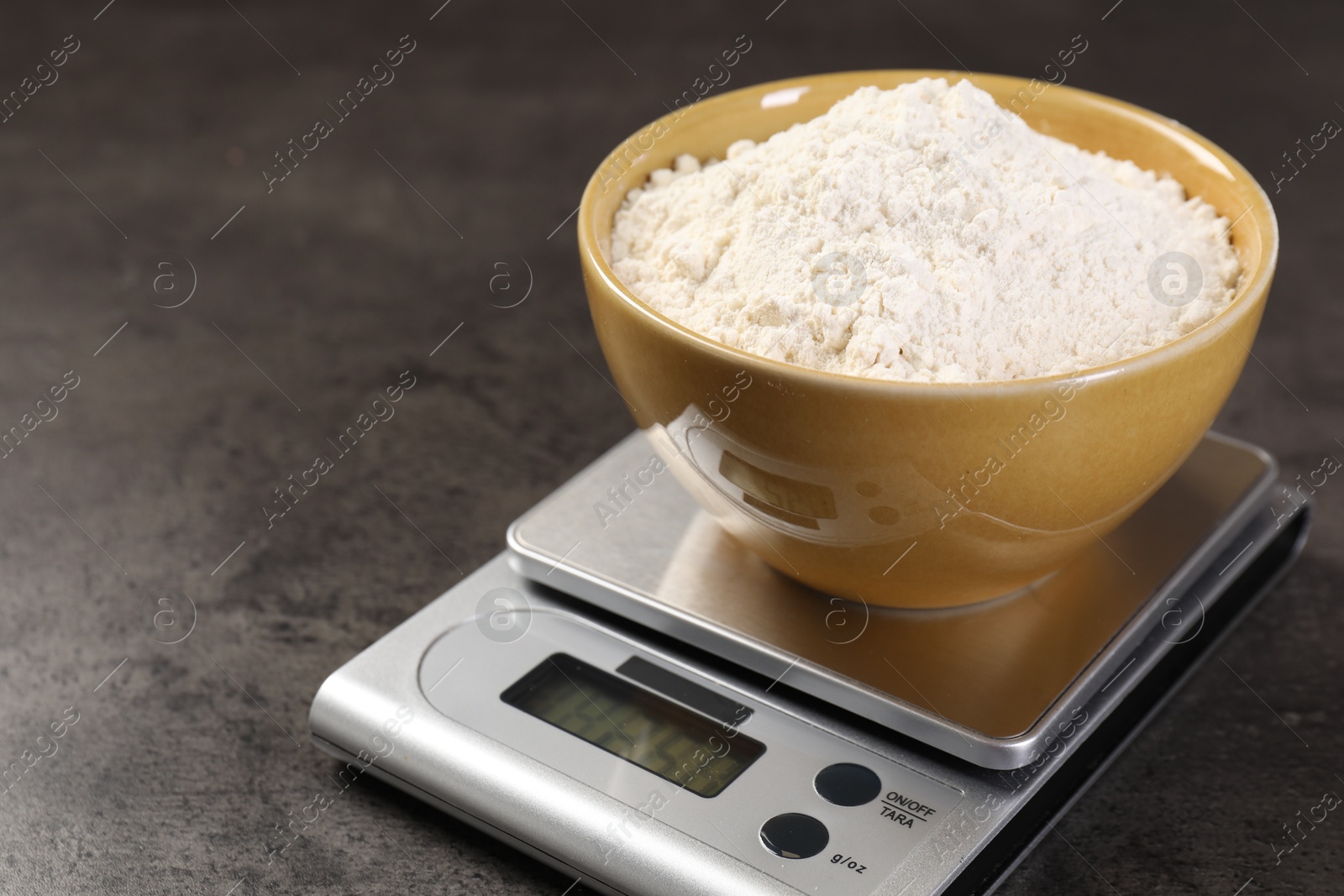 Digital kitchen scale with bowl of flour on grey table, closeup. Space for text Photo of Digital kitchen scale with bowl of flour on grey table, closeup. Space for text