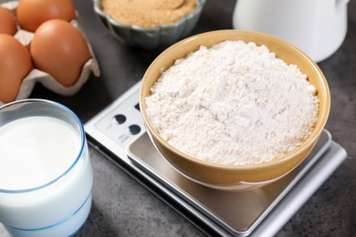 Photo of Digital kitchen scale with bowl of flour and other products on grey table, closeup
