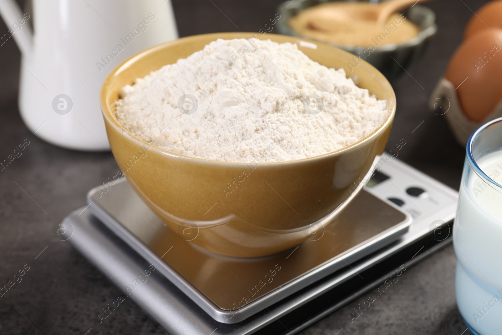 Photo of Digital kitchen scale with bowl of flour and other products on grey table, closeup
