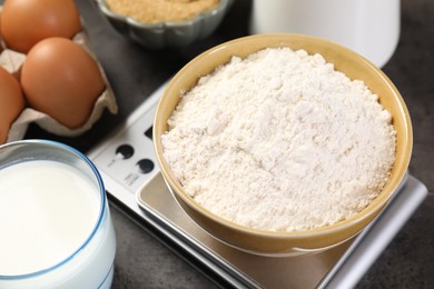 Photo of Digital kitchen scale with bowl of flour and other products on grey table, closeup