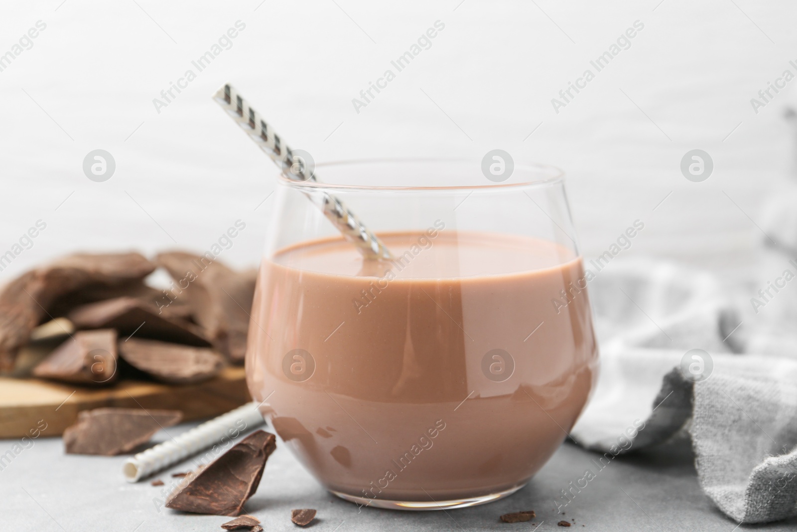 Tasty chocolate milk in glass and pieces of chocolate on light grey table, closeup Photo of Tasty chocolate milk in glass and pieces of chocolate on light grey table, closeup
