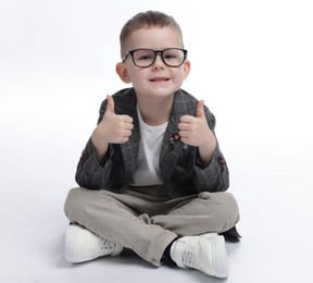 Photo of Cute little boy in glasses showing thumbs up on white background