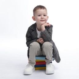 Photo of Cute little boy on books against white background