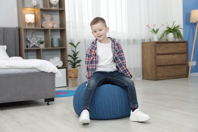Photo of Cute little boy sitting on pouf at home