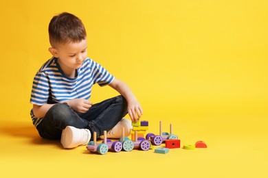 Photo of Cute little boy playing on yellow background, space for text