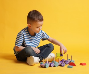 Photo of Cute little boy playing with train toy on yellow background