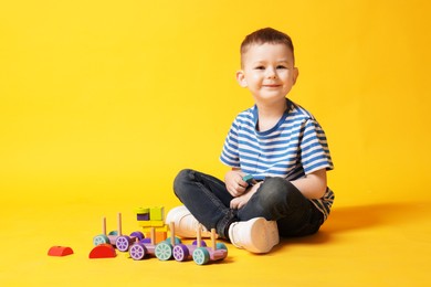 Photo of Cute little boy with toys on yellow background