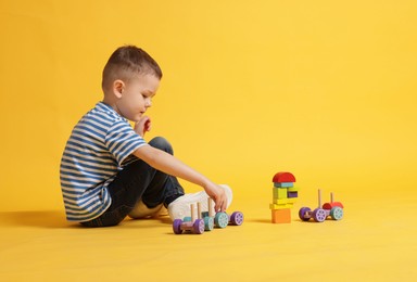 Photo of Cute little boy playing with train toy on yellow background