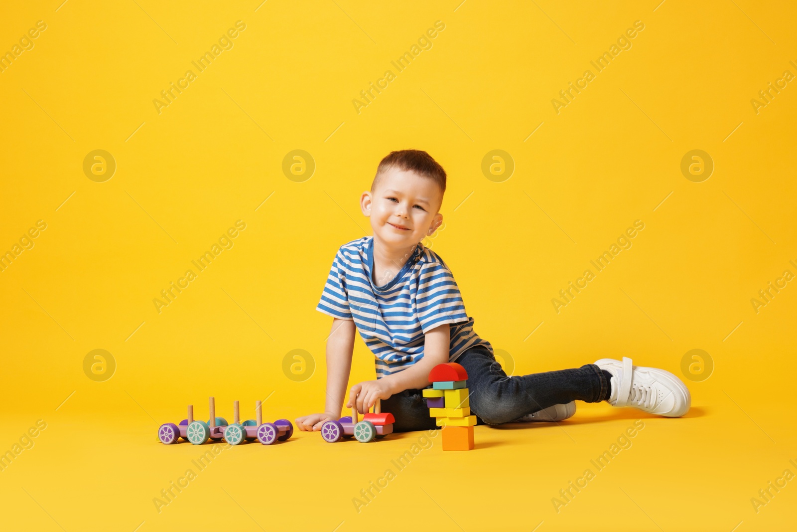 Cute little boy playing with train toy on yellow background Photo of Cute little boy playing with train toy on yellow background