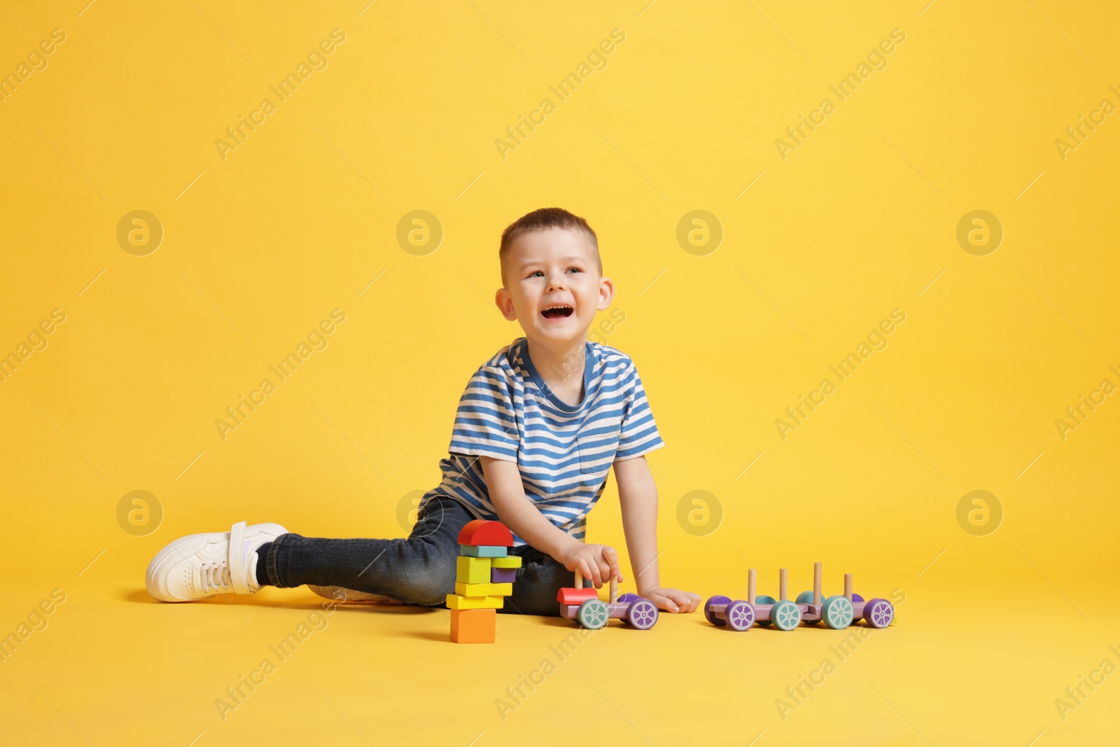 Cute little boy playing with train toy on yellow background Photo of Cute little boy playing with train toy on yellow background