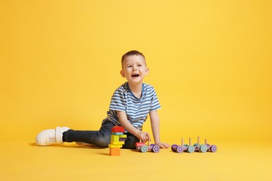 Photo of Cute little boy playing with train toy on yellow background
