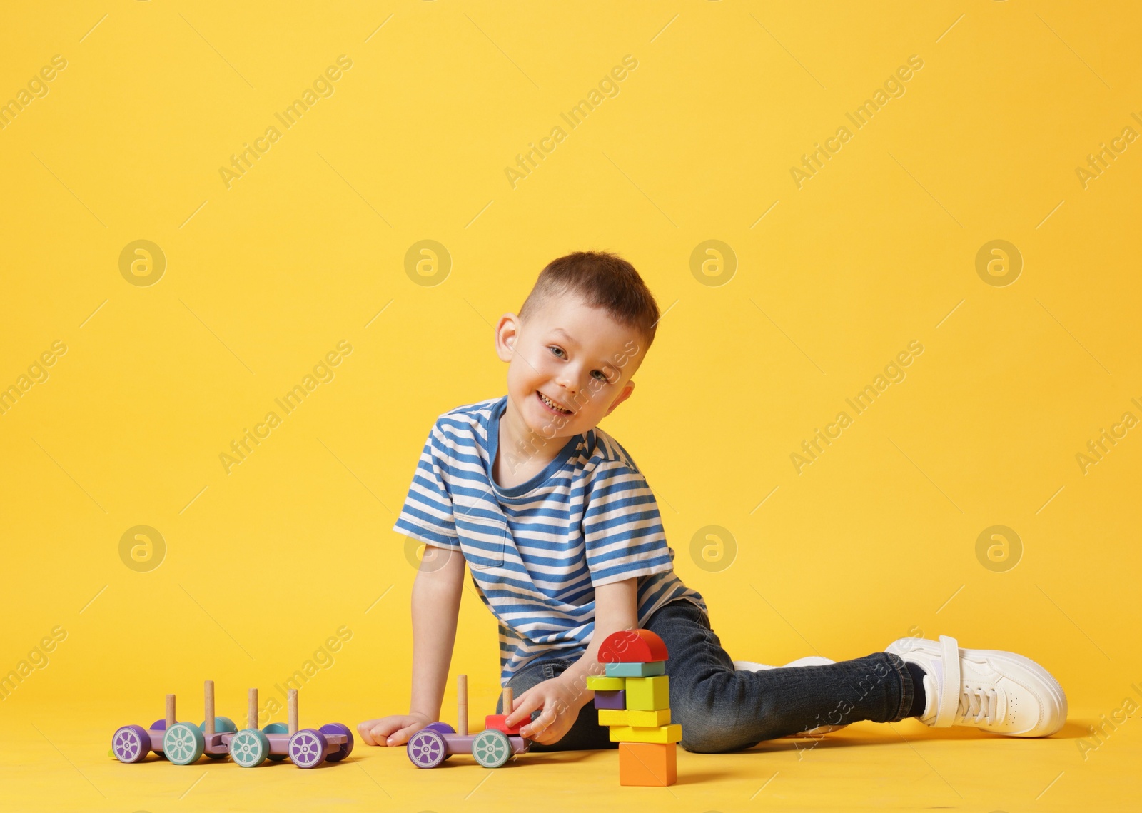 Cute little boy playing with train toy on yellow background Photo of Cute little boy playing with train toy on yellow background