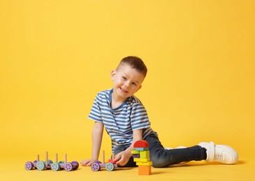 Photo of Cute little boy playing with train toy on yellow background