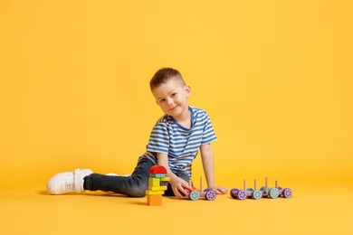 Photo of Cute little boy playing with train toy on yellow background