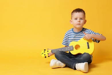Photo of Cute little boy playing toy guitar on yellow background, space for text