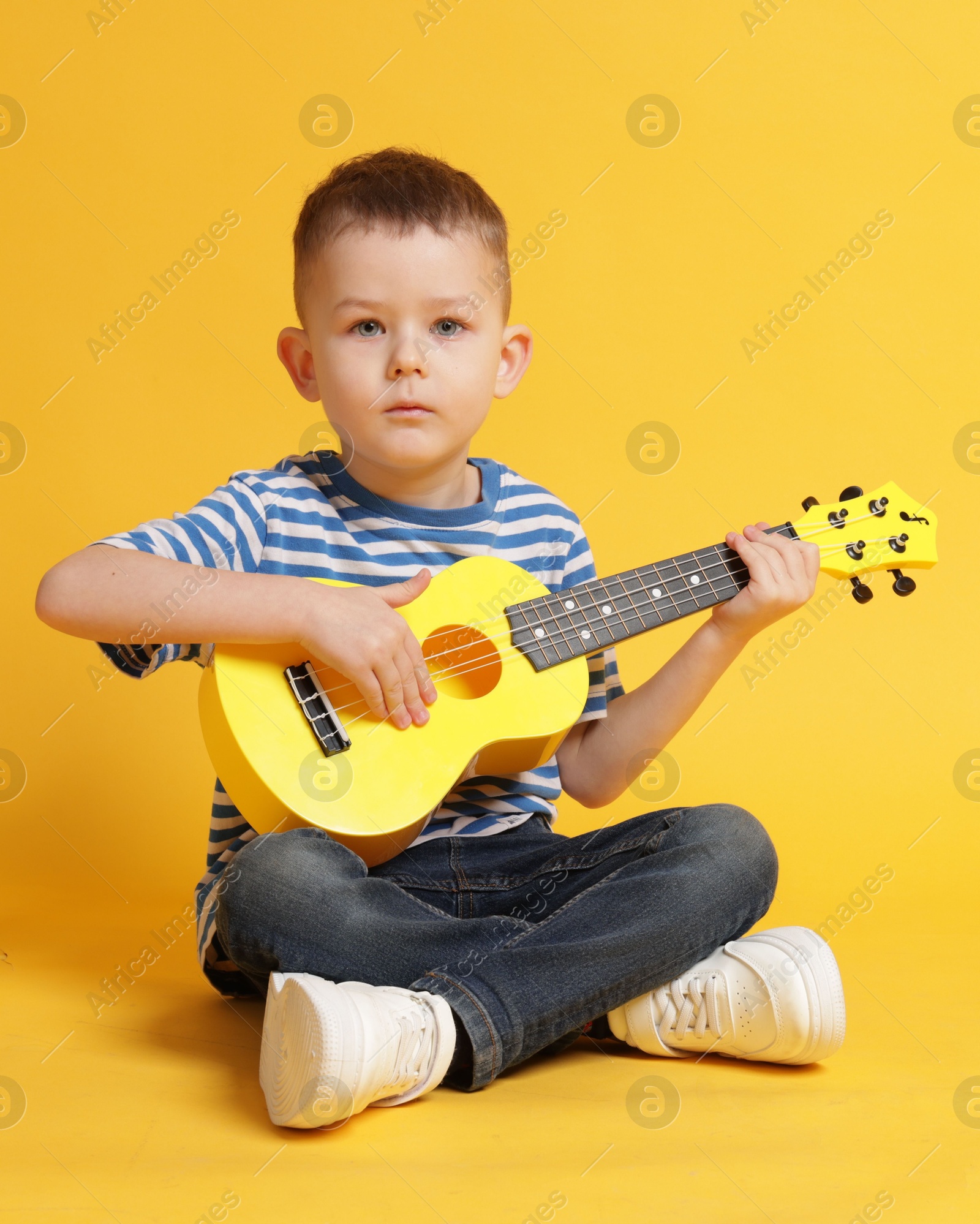 Cute little boy playing toy guitar on yellow background Photo of Cute little boy playing toy guitar on yellow background