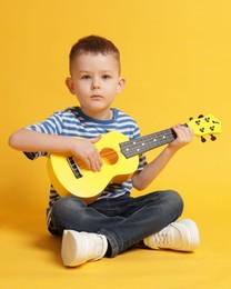 Photo of Cute little boy playing toy guitar on yellow background