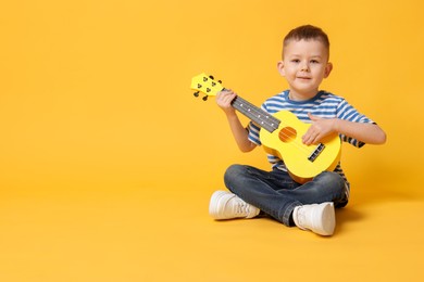 Photo of Cute little boy playing toy guitar on yellow background, space for text