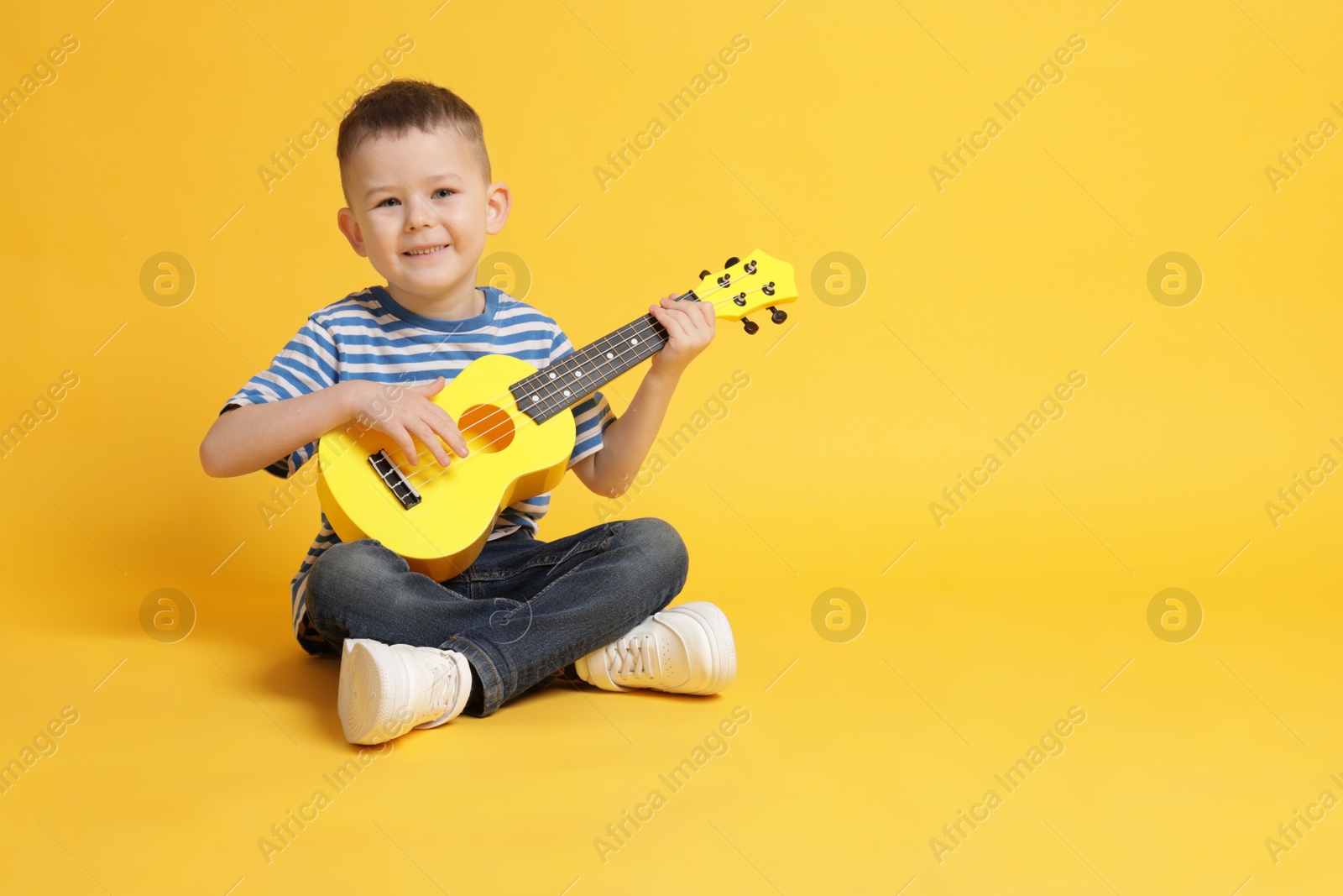 Cute little boy playing toy guitar on yellow background, space for text Photo of Cute little boy playing toy guitar on yellow background, space for text