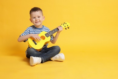 Photo of Cute little boy playing toy guitar on yellow background, space for text