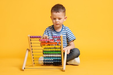 Photo of Cute little boy playing with wooden abacus on yellow background