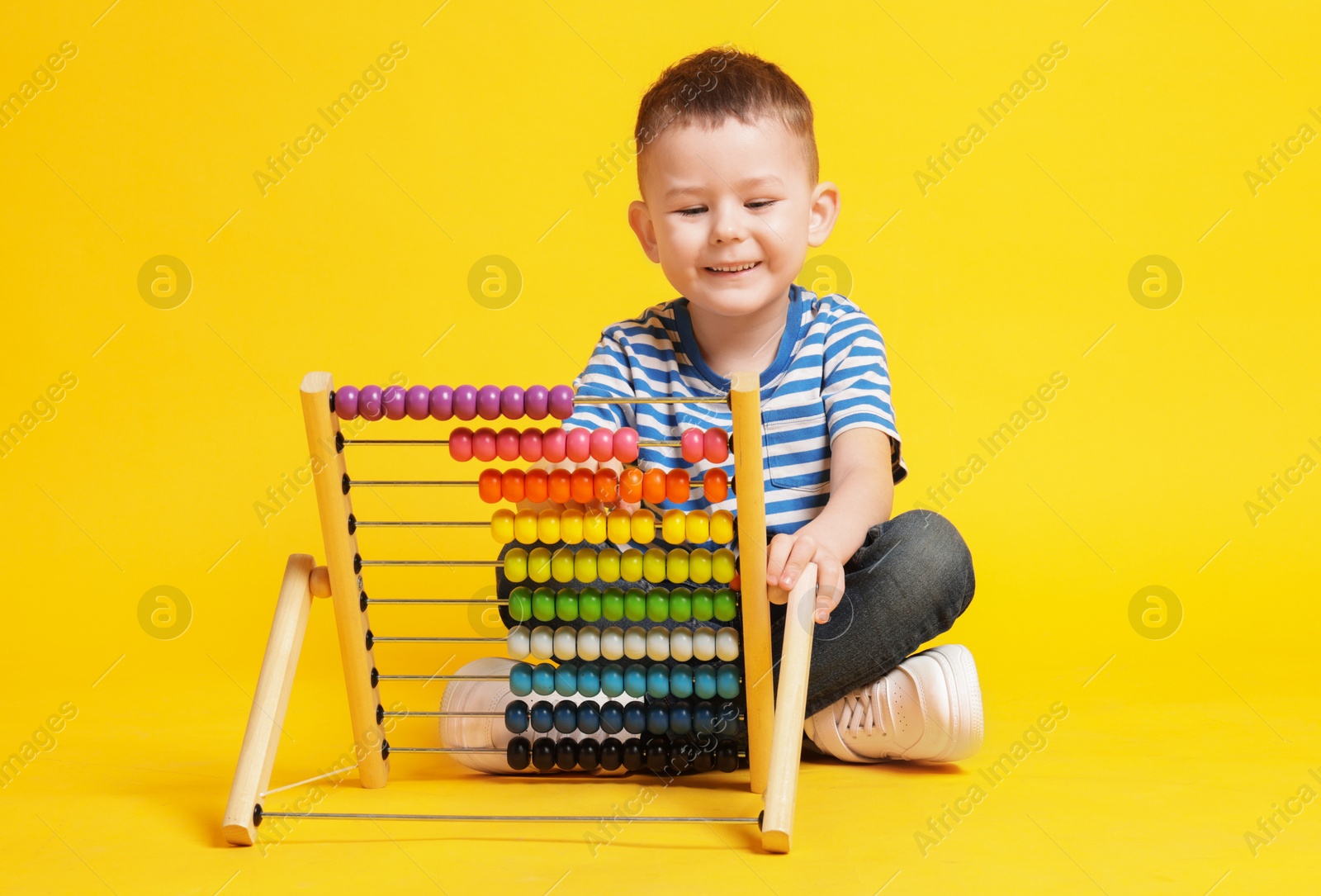 Cute little boy playing with wooden abacus on yellow background Photo of Cute little boy playing with wooden abacus on yellow background
