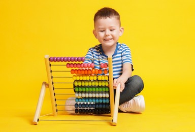 Photo of Cute little boy playing with wooden abacus on yellow background