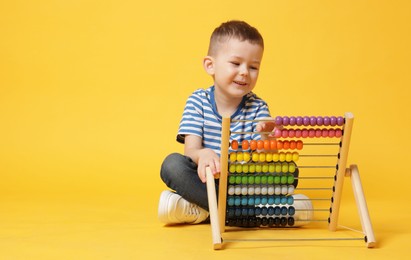 Photo of Cute little boy playing with wooden abacus on yellow background, space for text