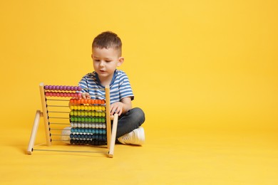 Photo of Cute little boy playing with wooden abacus on yellow background, space for text
