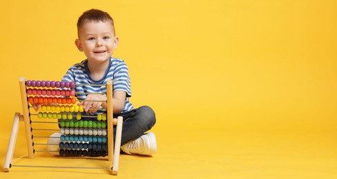 Photo of Cute little boy playing with wooden abacus on yellow background, space for text