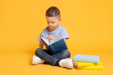 Photo of Cute little boy reading book on yellow background