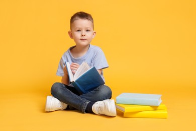 Photo of Cute little boy with book on yellow background