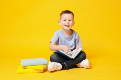 Photo of Cute little boy with book on yellow background