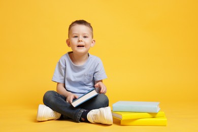 Photo of Cute little boy with book on yellow background