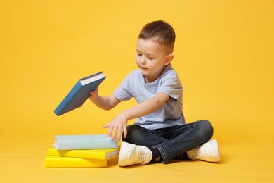 Photo of Cute little boy with books on yellow background