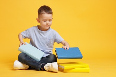 Photo of Cute little boy with books on yellow background