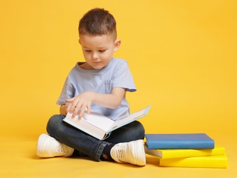 Photo of Cute little boy reading book on yellow background