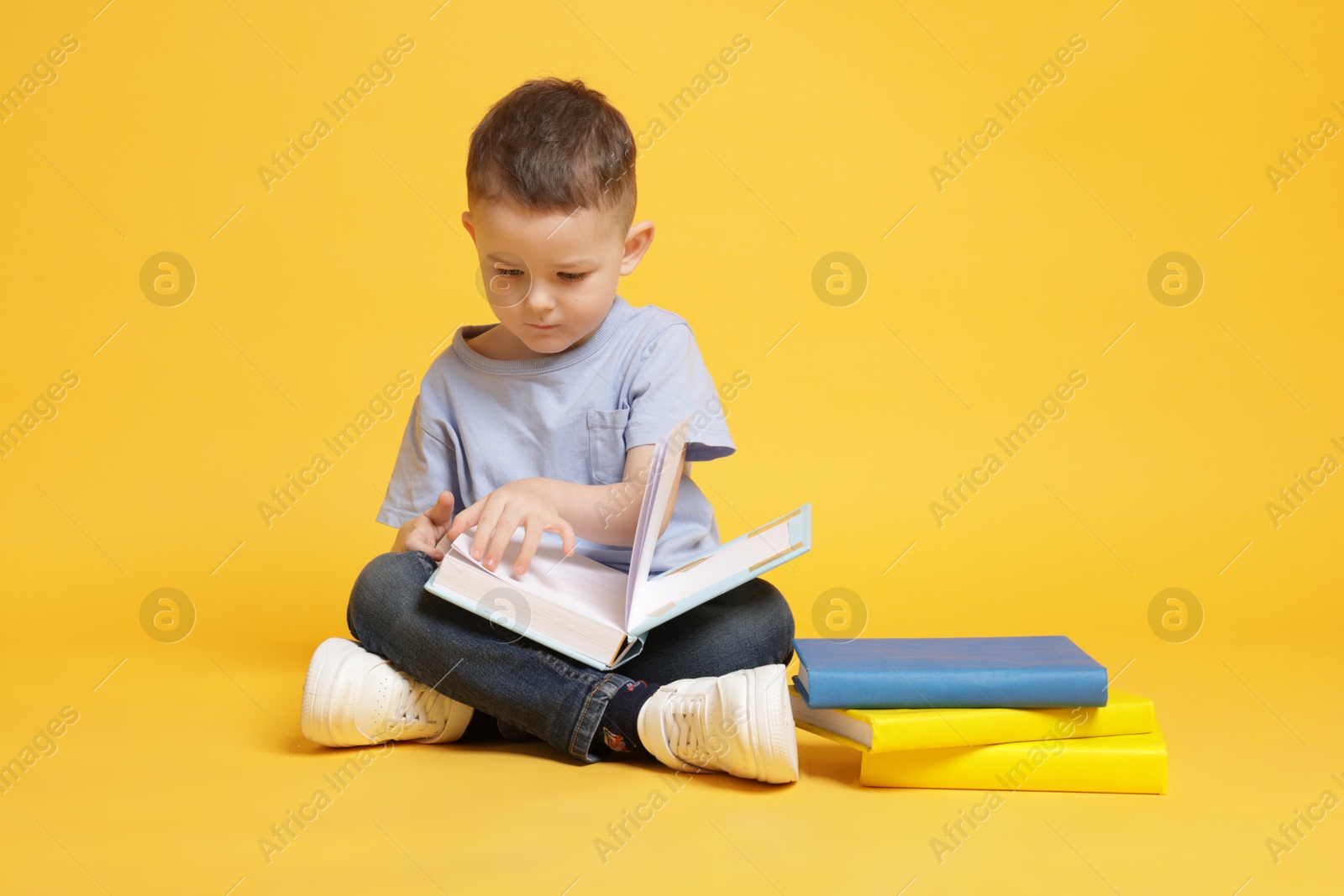Cute little boy reading book on yellow background Photo of Cute little boy reading book on yellow background